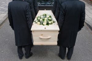 Individuals solemnly transporting a coffin into a vehicle.