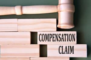 Wooden blocks with the words "Compensation Claim" next to a judge's gavel, symbolizing legal action for personal injury or damages.